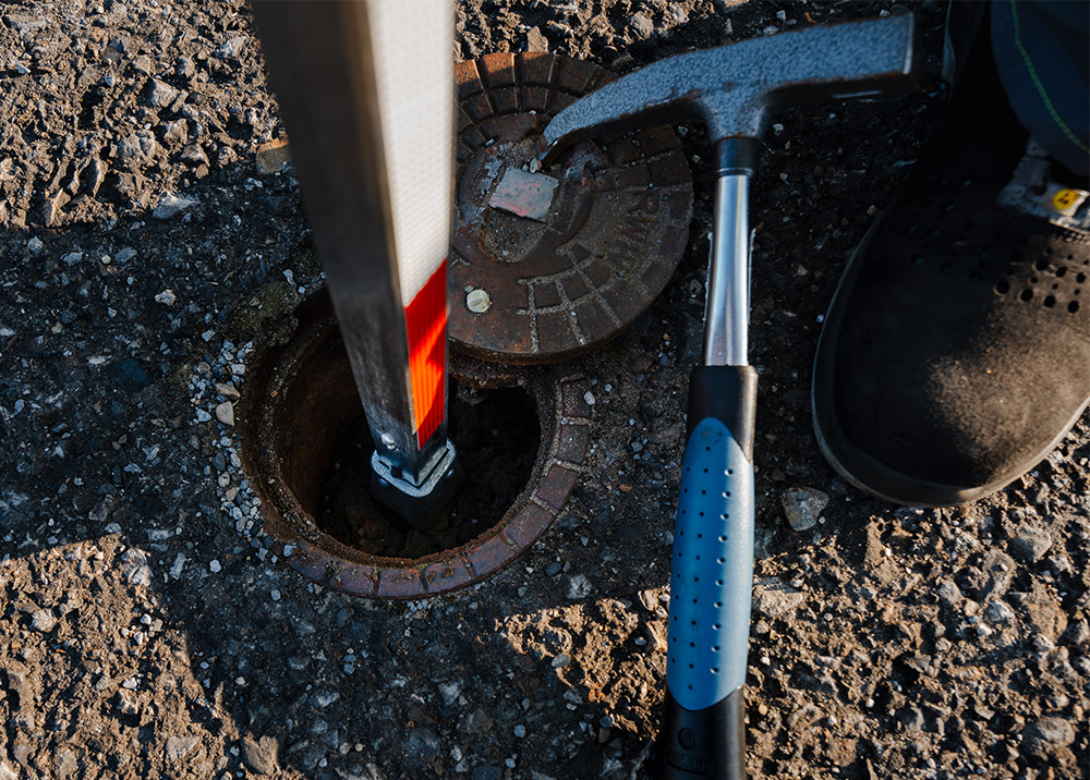 Traffic post is set into a curb, next to a hammer and a black shoe on an asphalt road.
