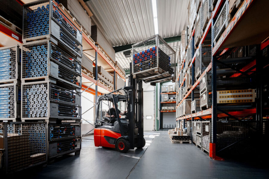 Gabelstapler bewegt eine Metallkiste in einem Lager voller Regale mit gelagerten Waren, industrielles Umfeld, hohe Decke, logistischer Betrieb.